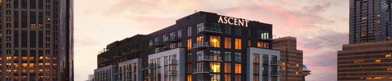 Dusk skyline featuring 'ASCENT' residential building with illuminated windows, flanked by high-rise buildings.