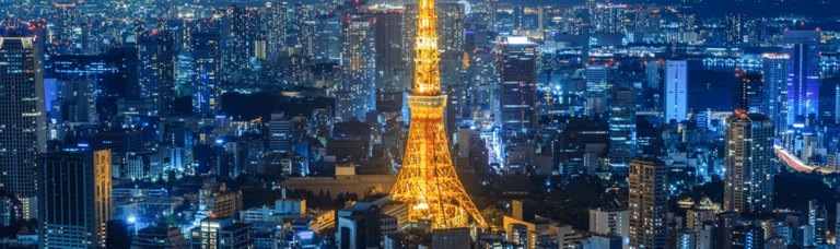 Night view of a vibrant cityscape with a prominent illuminated tower at the center, surrounded by a myriad of glowing buildings.