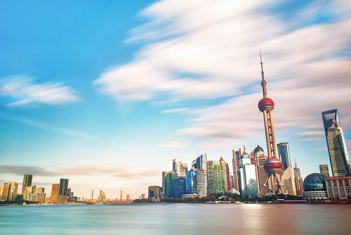 Time-lapse view of a vibrant city skyline featuring iconic futuristic towers and skyscrapers, with streaks of clouds in the sky above.