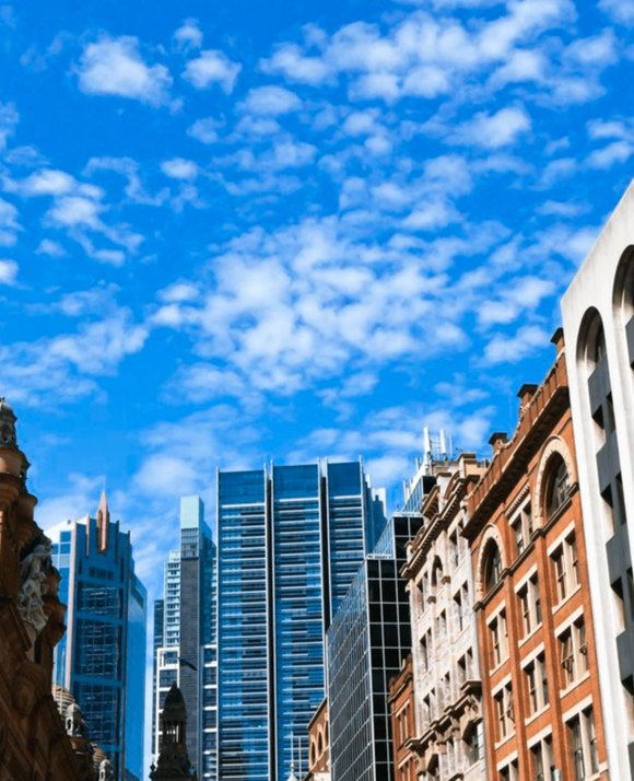 Contrast of architectural styles with historic red-brick buildings in the foreground and modern glass skyscrapers against a blue sky with fluffy clouds.