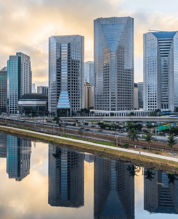 Reflective glass skyscrapers along a waterfront in São Paulo, Brazil, with a mirrored reflection on the water's surface at dawn
