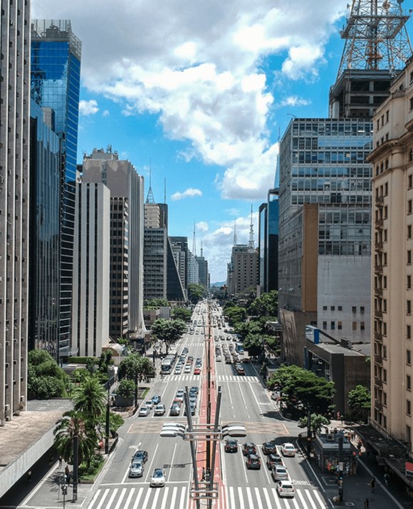 Aerial view of a bustling city avenue flanked by tall commercial buildings in São Paulo, Brazil, on a sunny day with scattered clouds.
