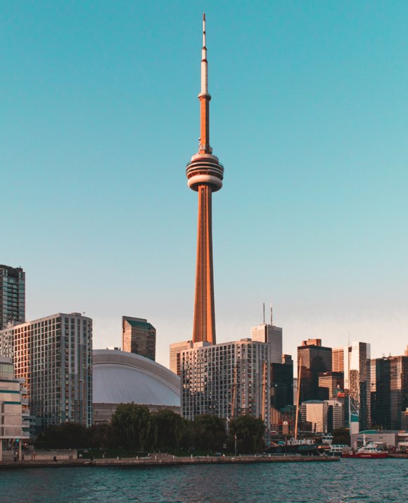 Iconic tall tower with a needle-like spire dominates the skyline, set against the backdrop of a waterfront cityscape during sunset.