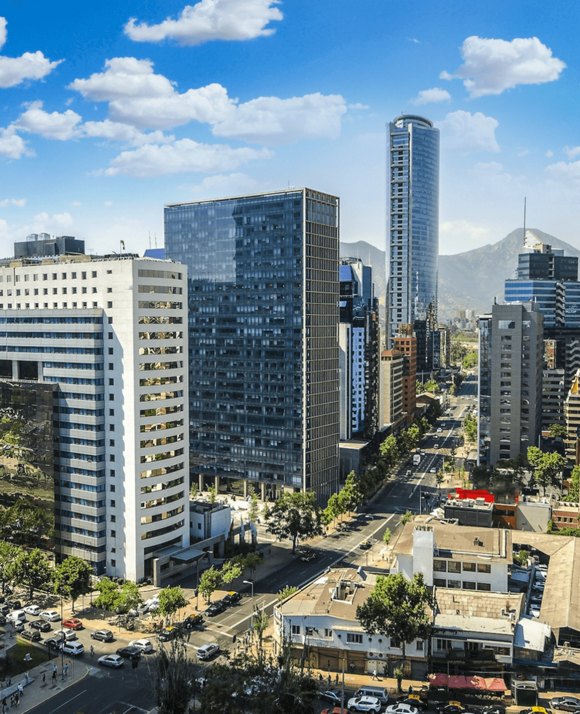 A vertical cityscape of Santiago, Chile, featuring modern high-rise buildings and bustling streets, with mountains in the distance under a blue sky.