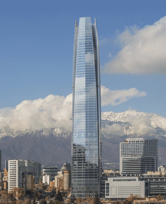 The Gran Torre Santiago skyscraper standing tall against the backdrop of the snow-capped Andes Mountains under a partly cloudy sky.