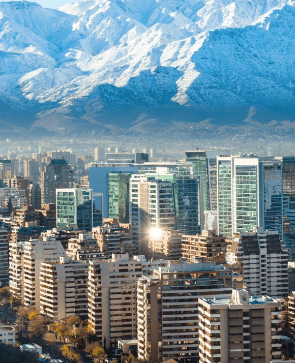 Cityscape with modern high-rise buildings in the foreground, reflecting the sunlight, against a backdrop of snow-capped mountains.