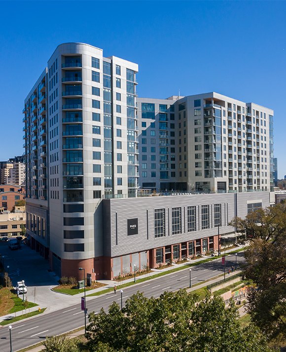 Contemporary multi-story apartment building with a curved corner design and ground-level retail spaces, located in an urban area.