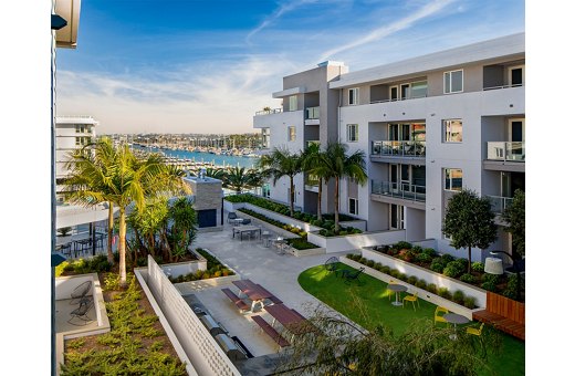 Luxury apartment complex courtyard with seating areas and lush landscaping, overlooking a marina.