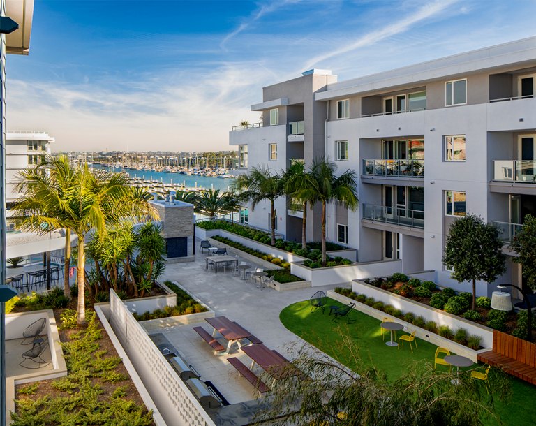 Luxury apartment complex courtyard with seating areas and lush landscaping, overlooking a marina.