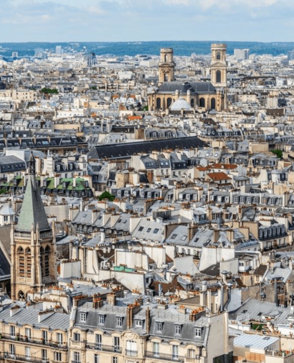 Expansive view of a historic city with dense traditional rooftops and prominent church steeples under a partly cloudy sky.