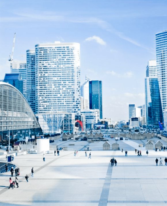 Spacious urban square with people walking, surrounded by modern high-rise buildings under a bright blue sky.