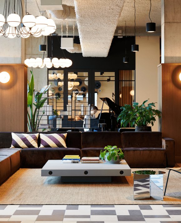 Stylish interior space with hanging orb lights, a dark brown sectional couch with striped pillows, and a view into a music room.