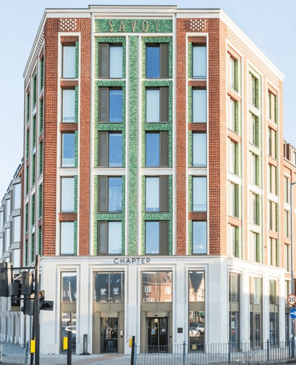 Facade of a modern building with a red brick exterior, green glazed terracotta tiles, and the word 'SAVOY' at the top, on a sunny day.