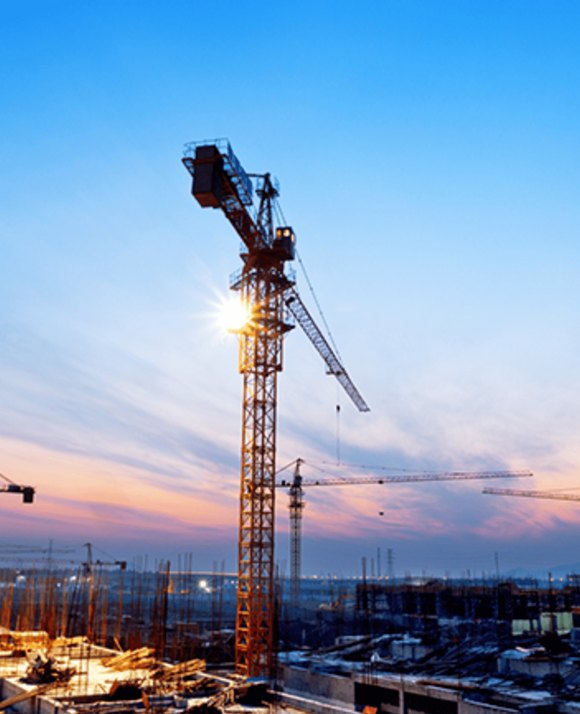 Silhouette of a construction crane at a building site against a sunset sky.