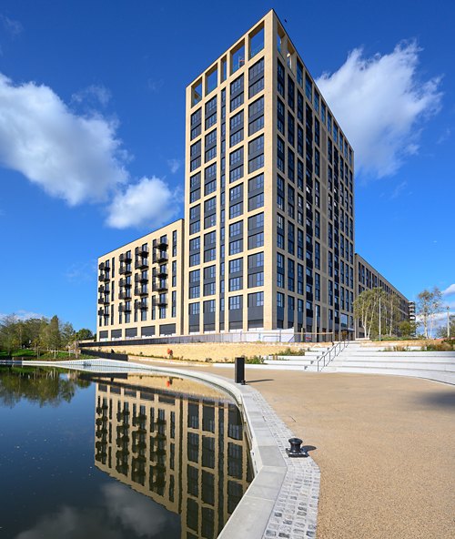 A tall, modern modular building with a contrasting trim, set against a clear blue sky and reflected in a still water feature.