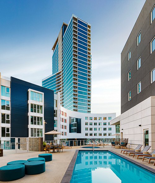 Swimming pool in a modern apartment complex courtyard, flanked by contemporary buildings with a tall glass skyscraper in the background.