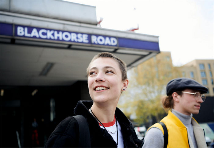 smiling young person standing in front of a Tube station