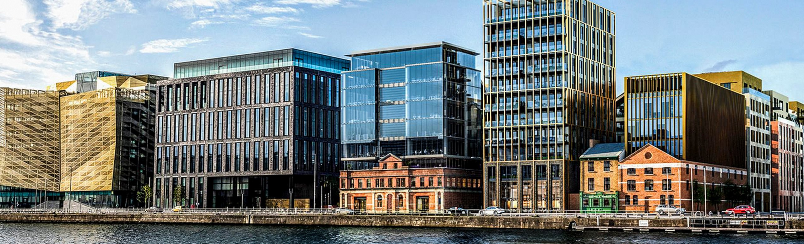 Waterside view of a modern mixed-use development with a variety of contemporary buildings, including a striking gold-colored structure.