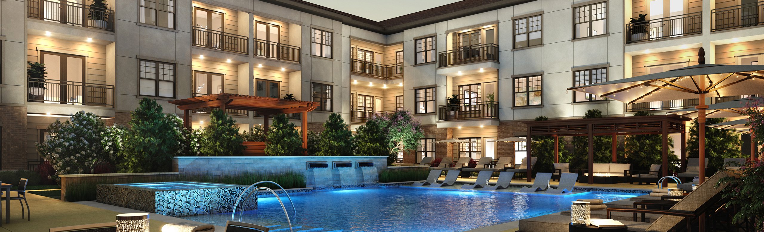 Evening view of a luxurious apartment complex with illuminated balconies overlooking a serene pool area with lounge chairs and a covered seating area.
