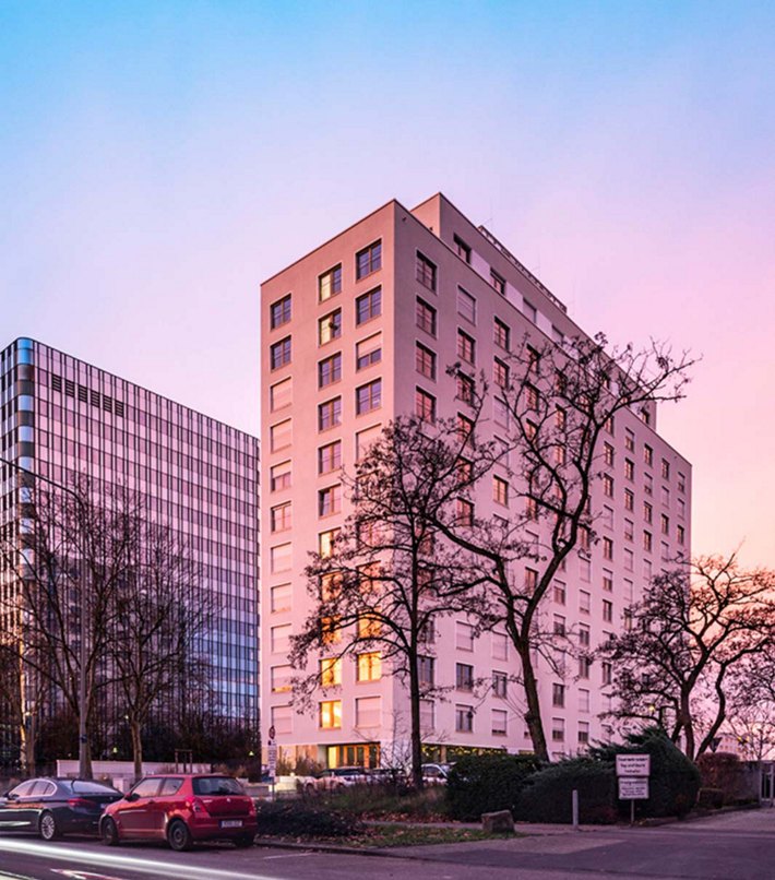 Panoramic view of a cityscape at dusk, showcasing modern high-rise buildings with reflective glass facades and a pastel-colored sky in the background.