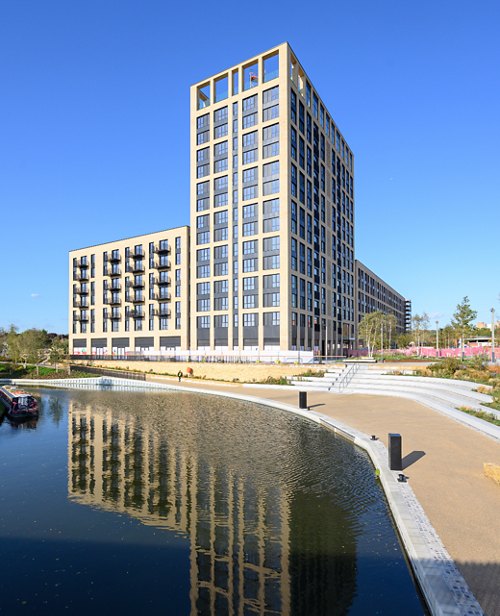 Modern residential building by a calm canal with clear reflections and a blue sky above.