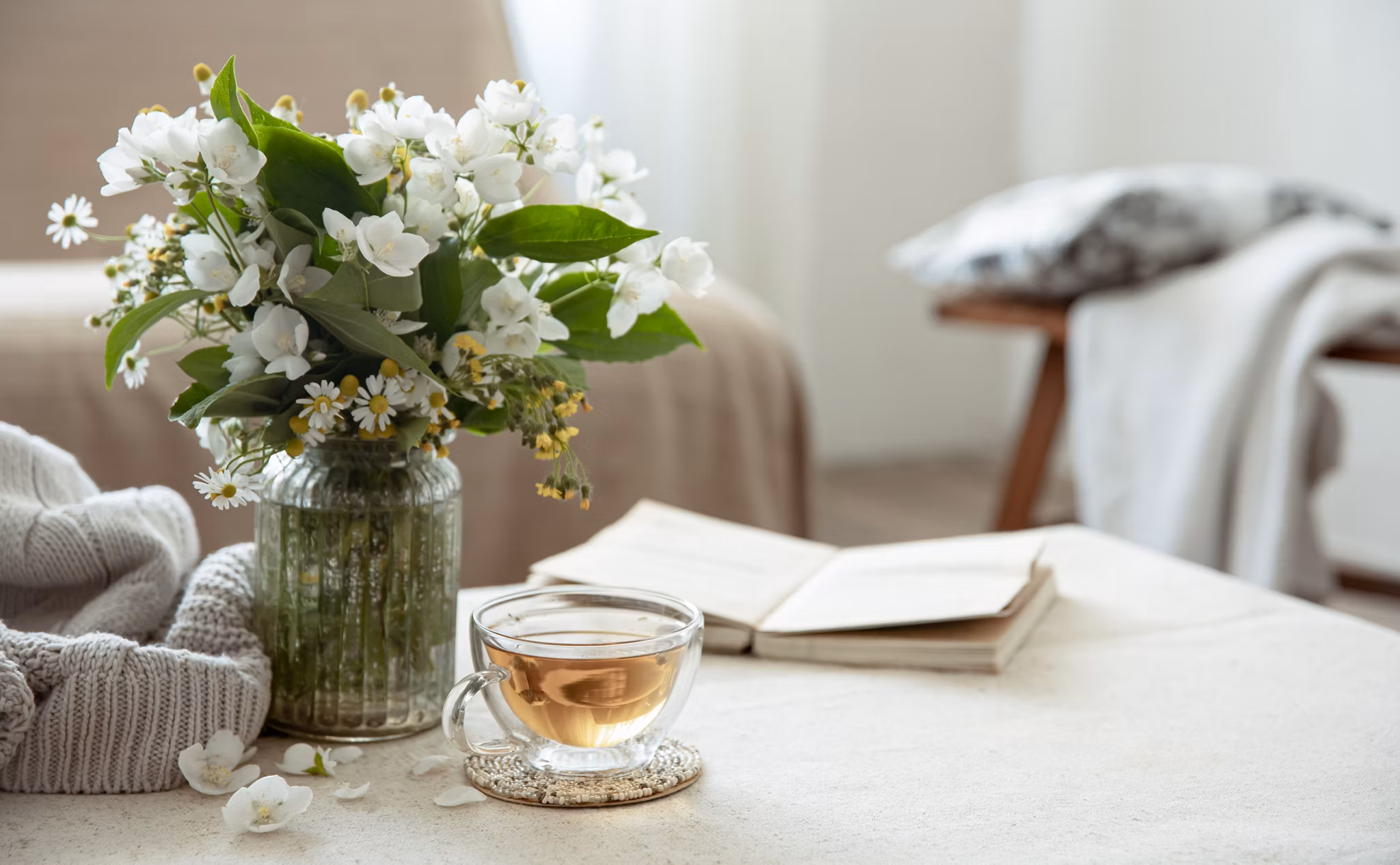Still life with a cup of herbal tea, a bouquet of flowers, a book and a knitted element on a blurred background.
