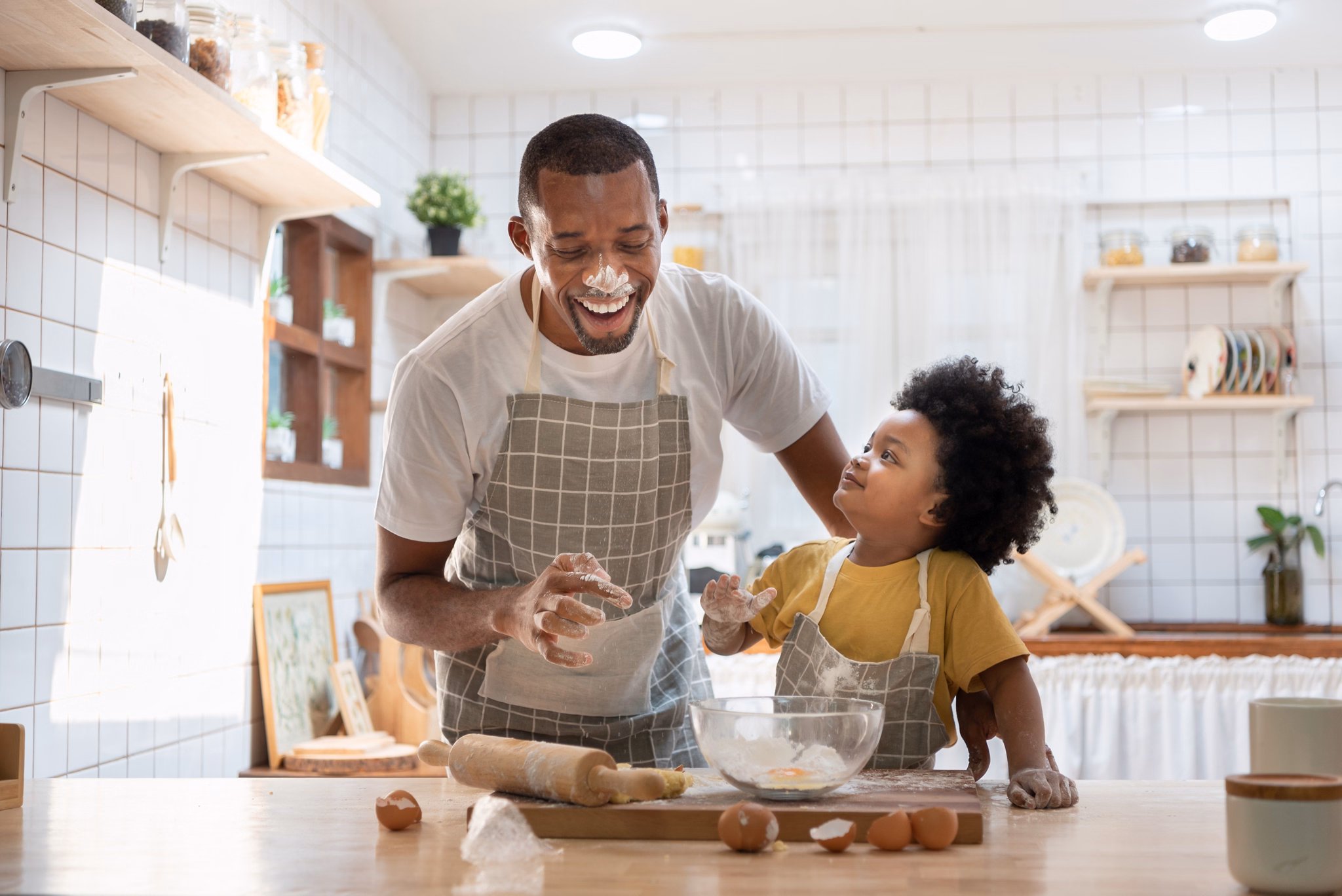 Cheerful smiling Black son enjoying playing with his father while doing bakery at home. Playful African family having fun cooking baking cake or cookies in kitchen together. Single Dad Lifestyle