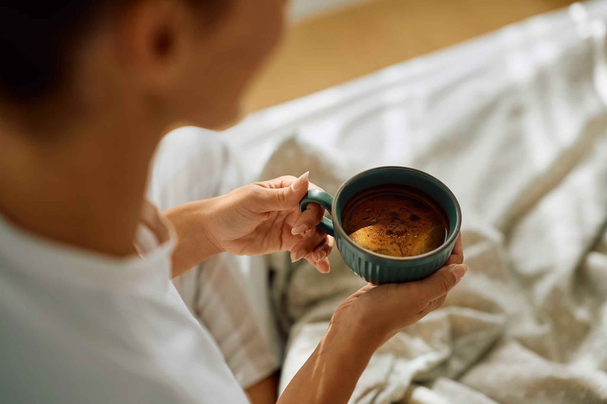 Close up of woman drinking coffee in bed in the morning.