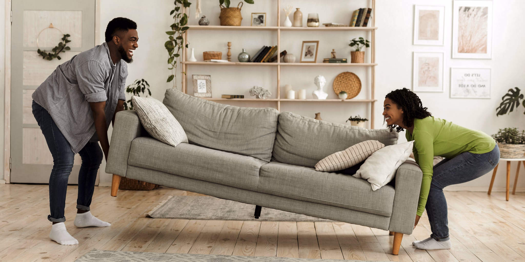 Happy african american couple moving sofa in living room, replacing furniture at home, side view