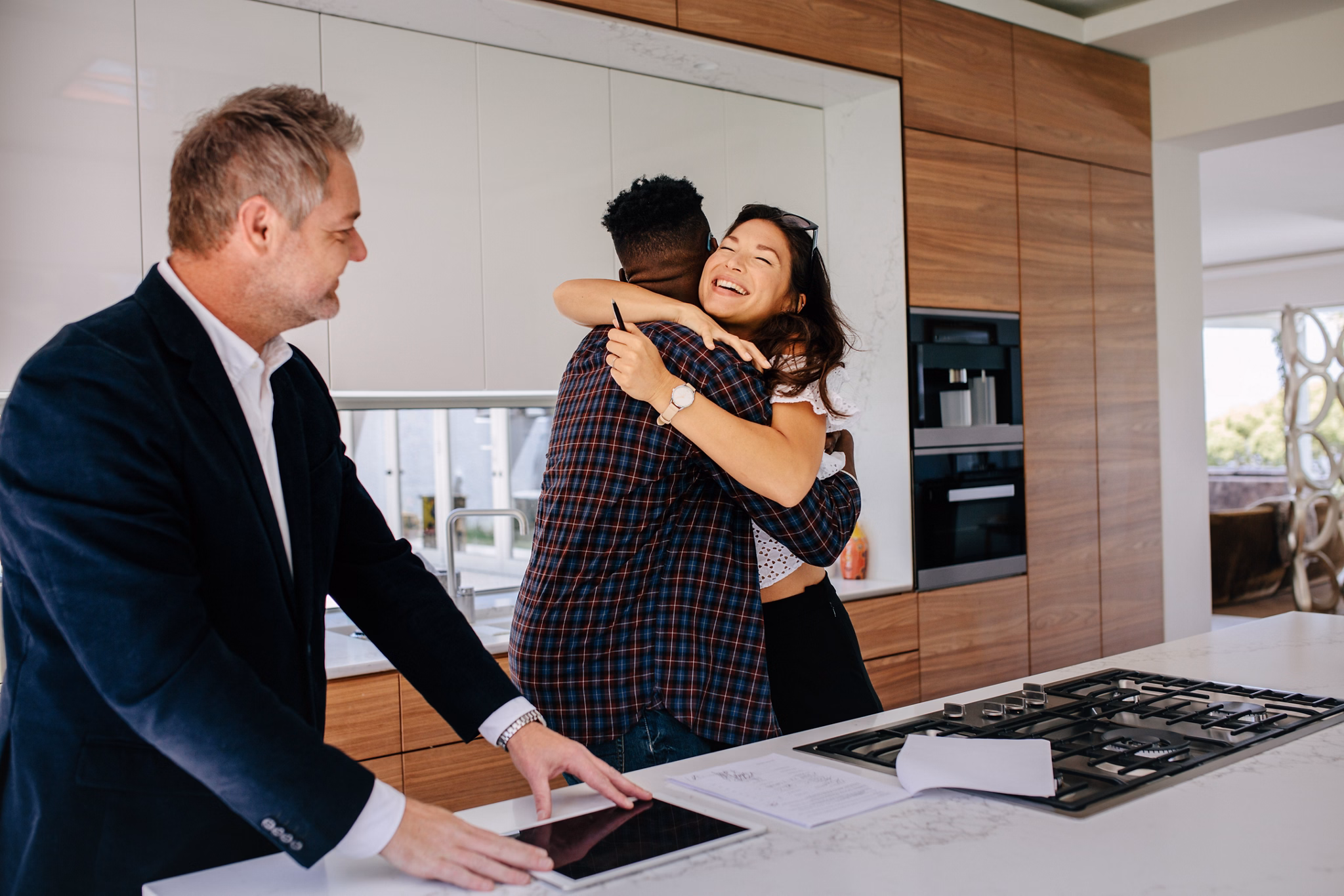 Excited couple hugging with real estate agent in kitchen of new home. Happy new property owners with realtor.
