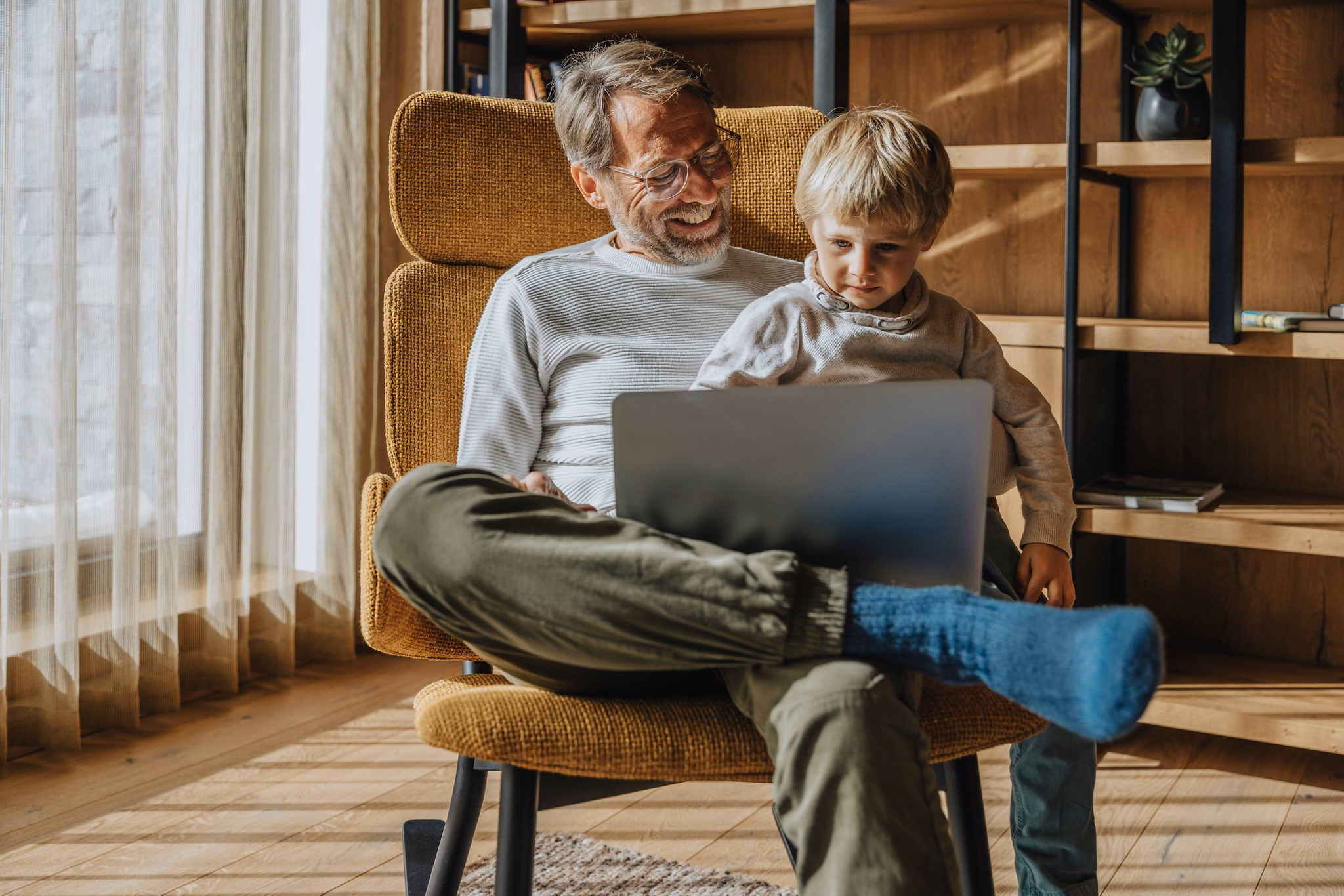 Vater und Sohn nutzen gemeinsam einen Laptop im Sessel, Maria Alm, Salzburger Land, Oesterreich