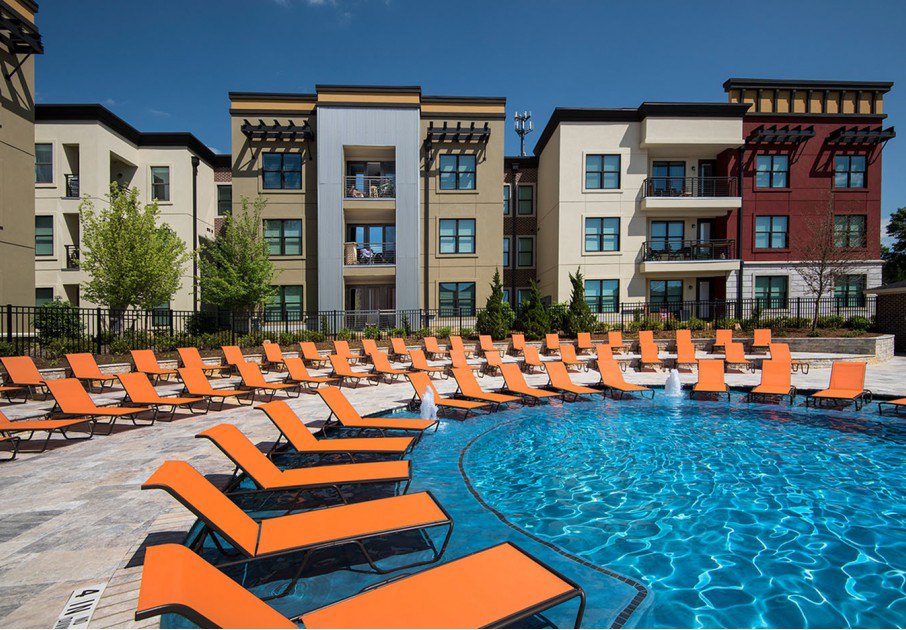 Outdoor pool area with bright orange lounge chairs at a modern apartment complex.