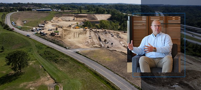 Aerial view of a large construction site with ongoing development, and an inset of a man speaking.