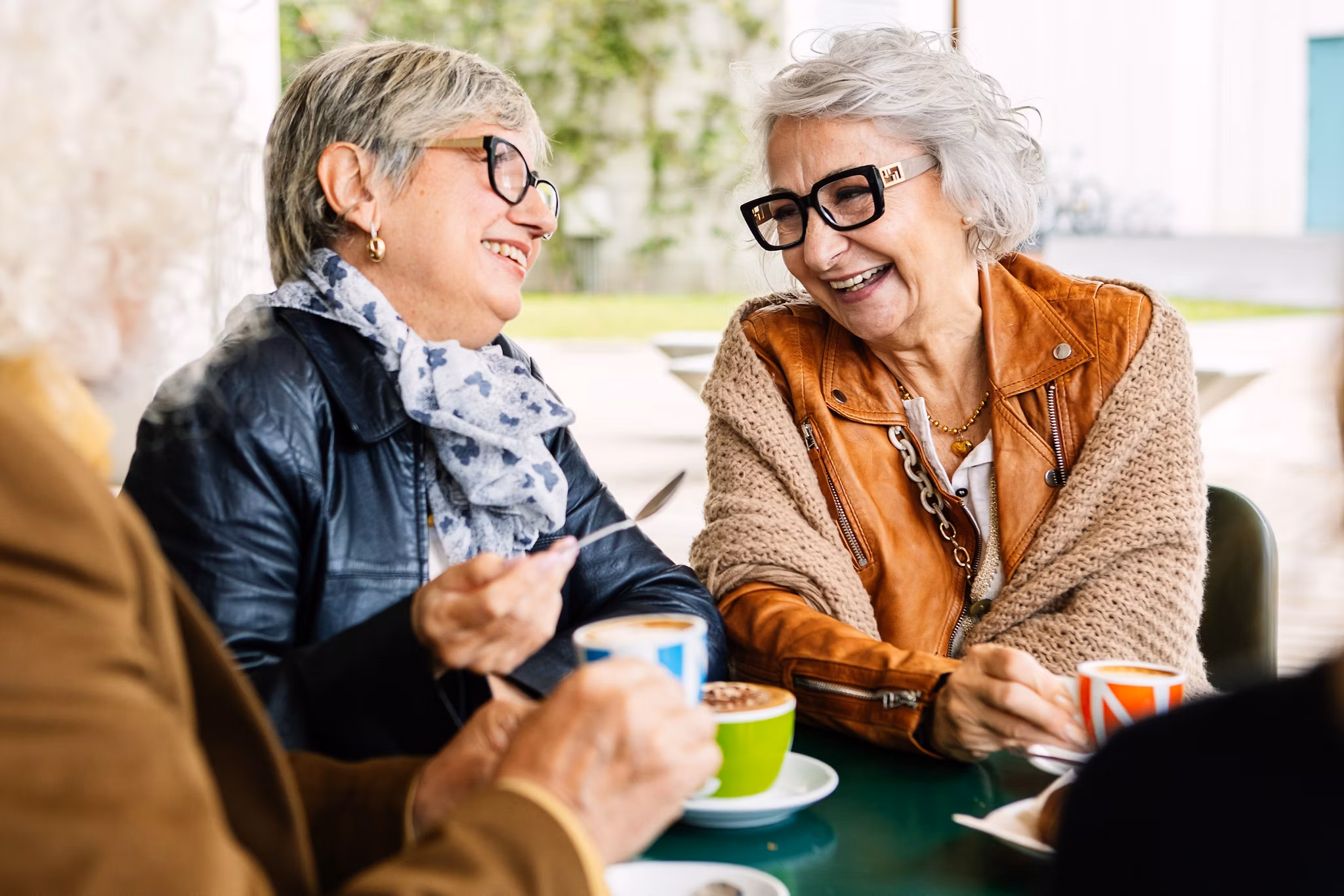 Senior women laughing while having breakfast with group of friends at cafeteria bar. Elderly lifestyle and friendship concept.