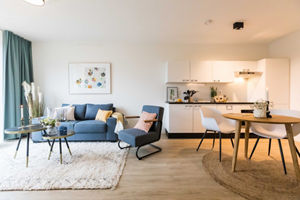 Stylish living room with a comfortable blue sofa, modern kitchenette, and a dining area with natural light.