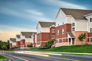 Exterior view of University Village Apartments on Colvin at Syracuse University, displaying a multi-story apartment complex with a mix of brick and siding finishes, surrounded by lush greenery and a clear sky