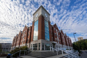 Exterior view of Ball & Chellgren Hall, a contemporary residence hall at the University of Kentucky, featuring a striking brick and glass exterior with large windows, set against a backdrop of a clear blue sky.