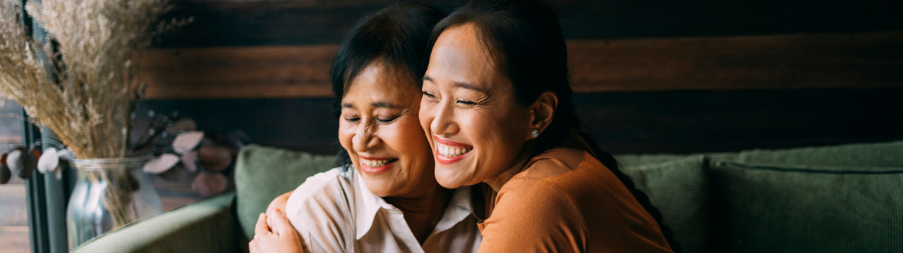 Asian mother and her daughter sitting on the sofa in their living room, spending time together.