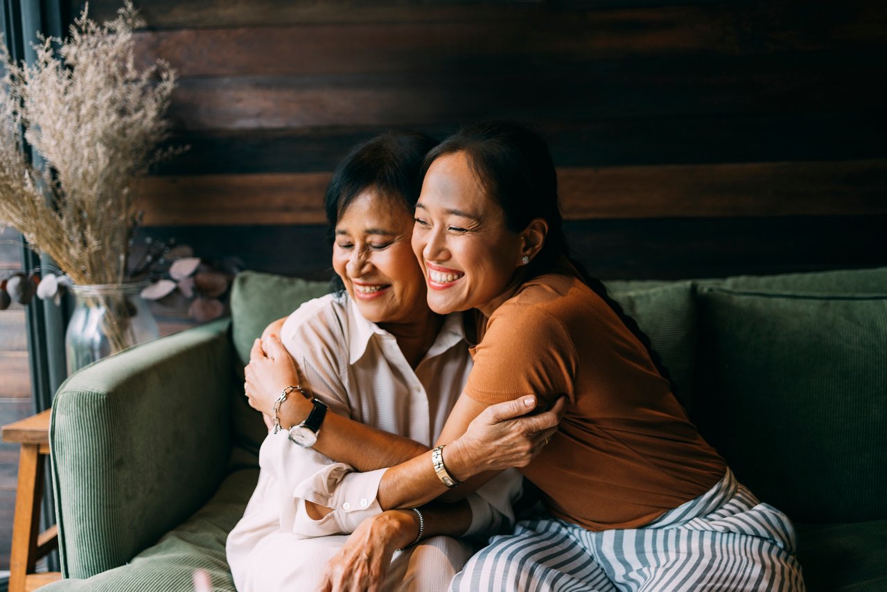 Asian mother and her daughter sitting on the sofa in their living room, spending time together.