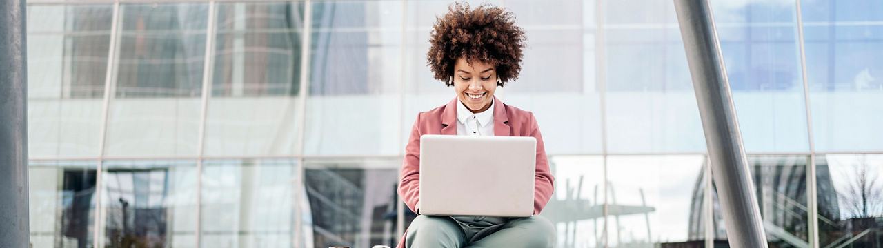 Business woman with wearing formal clothes sitting outdoors in business area and using her computer