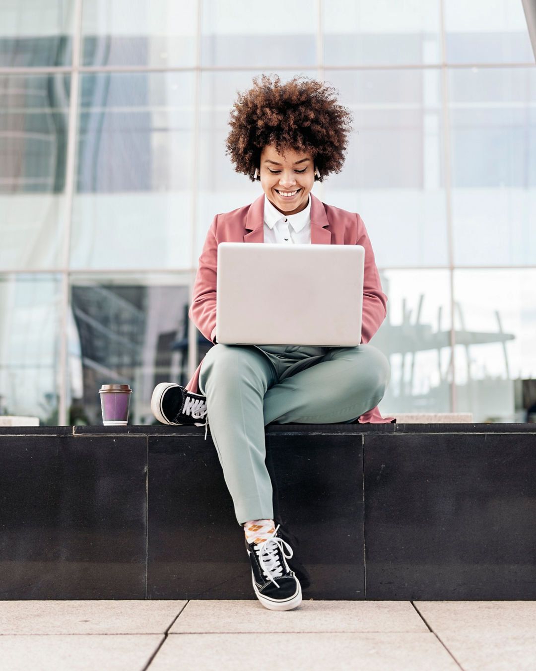 Business woman with wearing formal clothes sitting outdoors in business area and using her computer