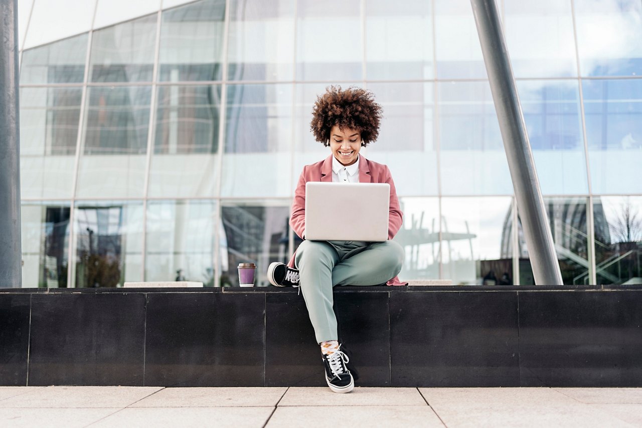 Business woman with wearing formal clothes sitting outdoors in business area and using her computer