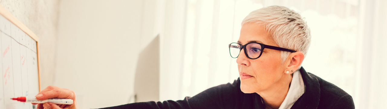 Mature businesswoman working in her home office. Standing by the desk and writing schedule. Selective focus on her face. Side view