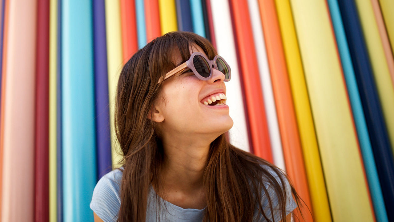 Close up portrait of cheerful young woman laughing with sunglasses against colourful background