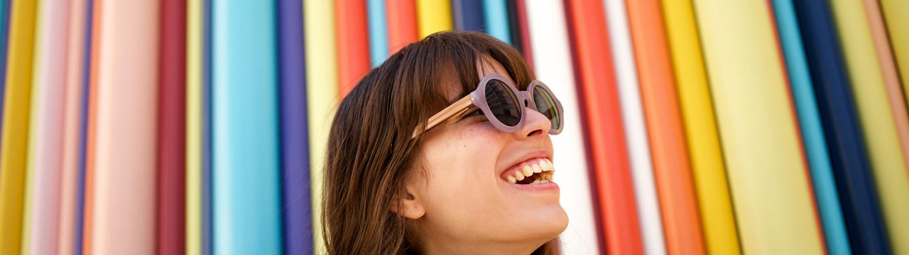 Close up portrait of cheerful young woman laughing with sunglasses against colourful background