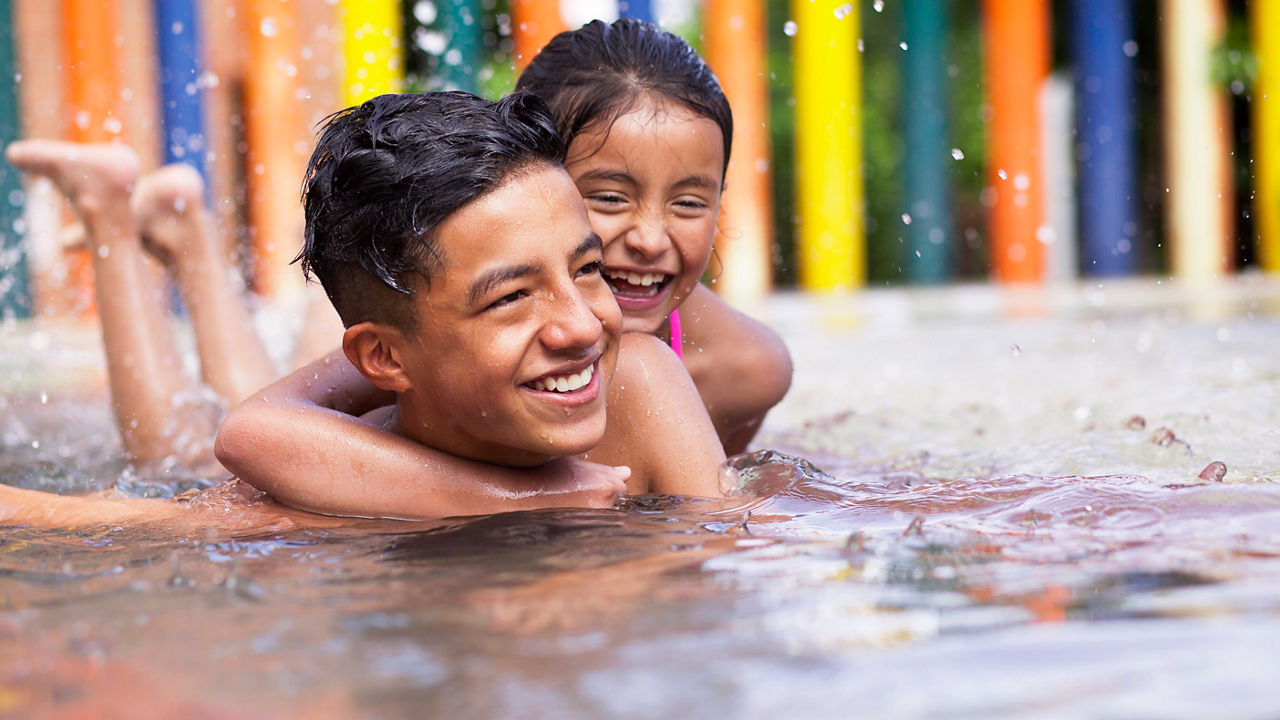 Latino children a teenage boy and an 8-year-old girl play in the pool, cuddle and cuddle in the water while smiling and having fun