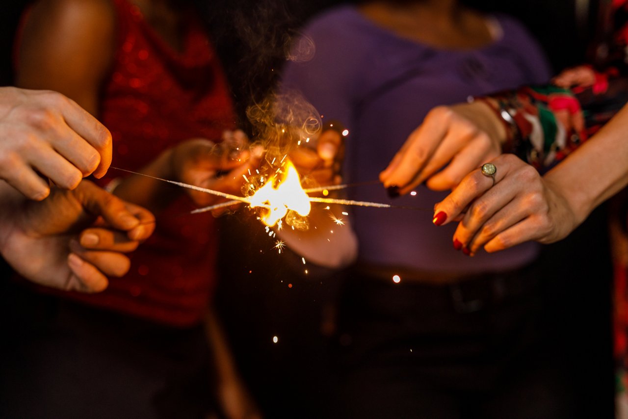 Close up shot of unrecognizable group of friends holding their sparklers together while igniting them during a fun New Year's eve party.