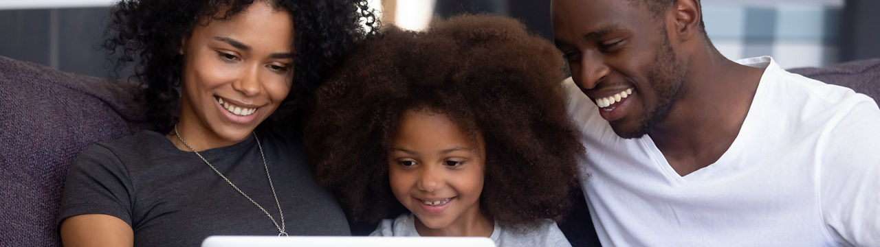 Happy African American family with child girl having fun using laptop together at home, black parents and little kid daughter watch funny video, do online shopping, make call look at computer screen