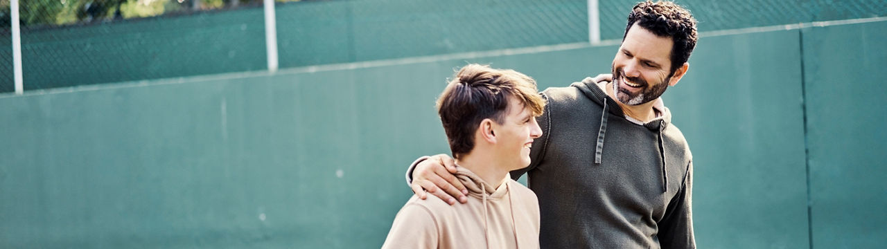 Father and son walking after playing a game of basketball. Young man and teenage boy having fun, talking and chatting while staying fit, active