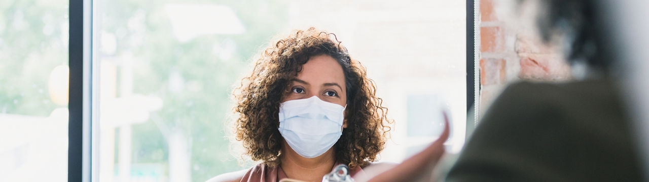 A confident female counselor attentively listens as a patient discusses something during a session. The counselor is wearing a protective mask as she is working during the COVID-19 pandemic. 